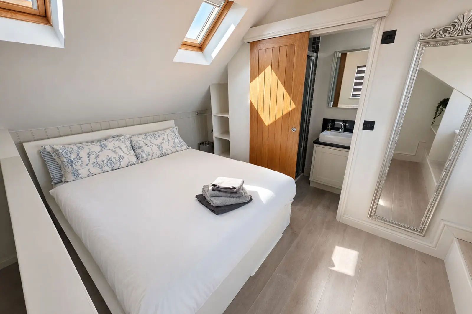 An attic conversion double bedroom well lit on a sunny day with the bed made up to hotel standard and towels laid out.