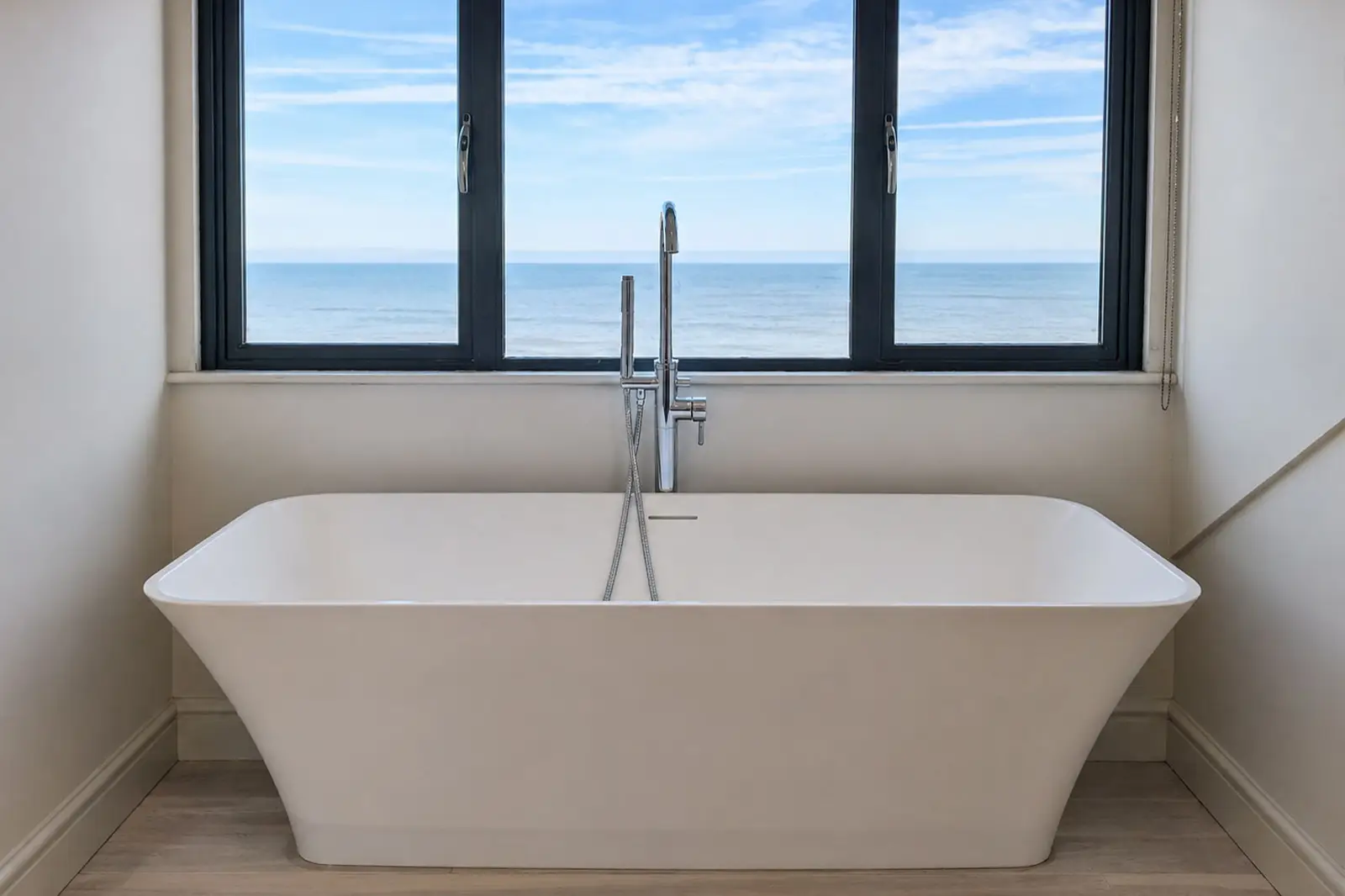 A free-standing bath tub positioned in front of a large window with views of Sheringham seafront.