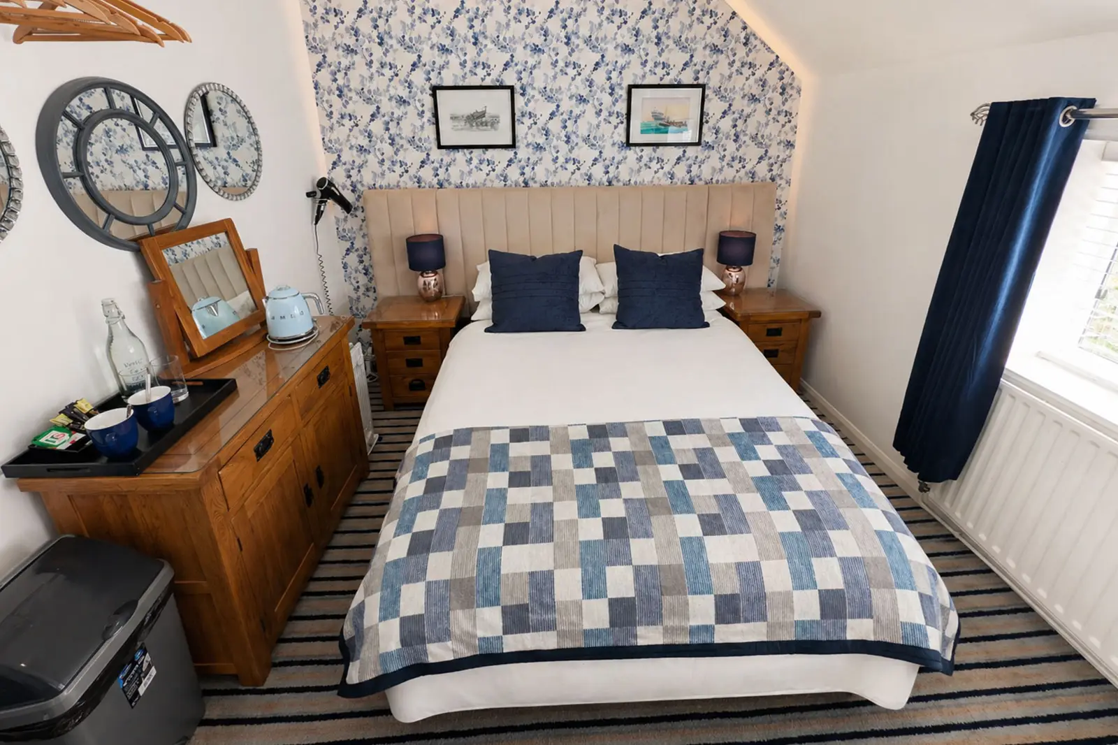 A twin bedroom with chequer pattern bedding, blue and white wallpaper, and a clock on the wall