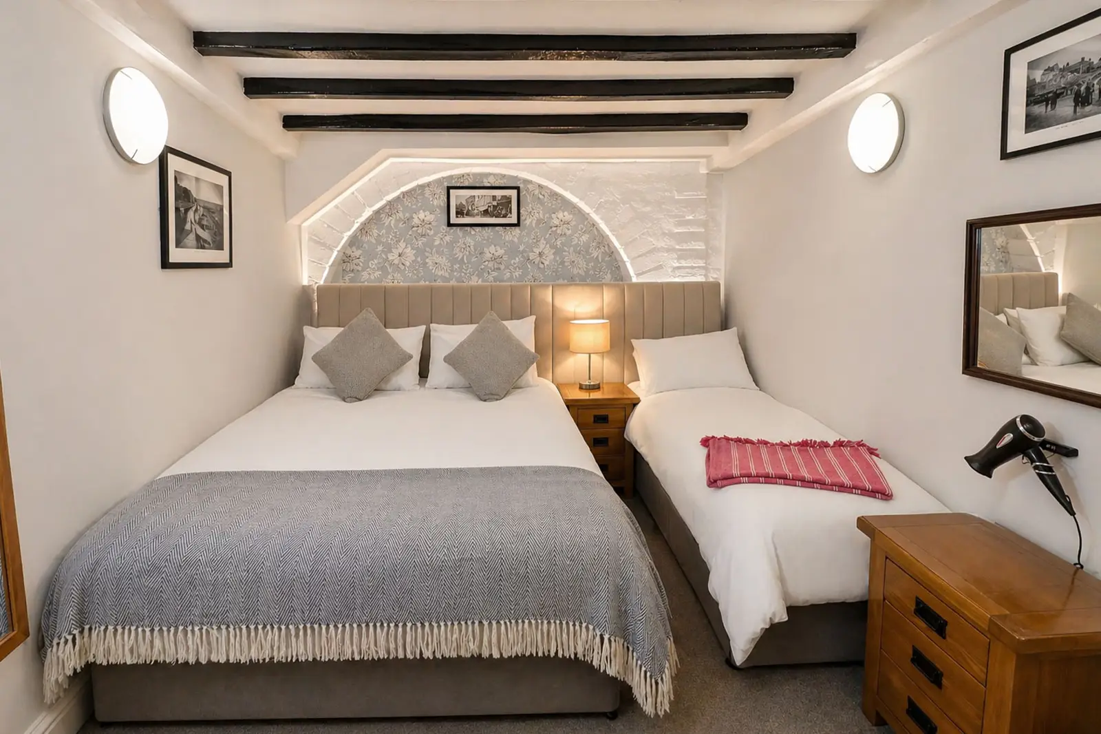 A double bed and single bed in a white room with exposed beams on the ceiling