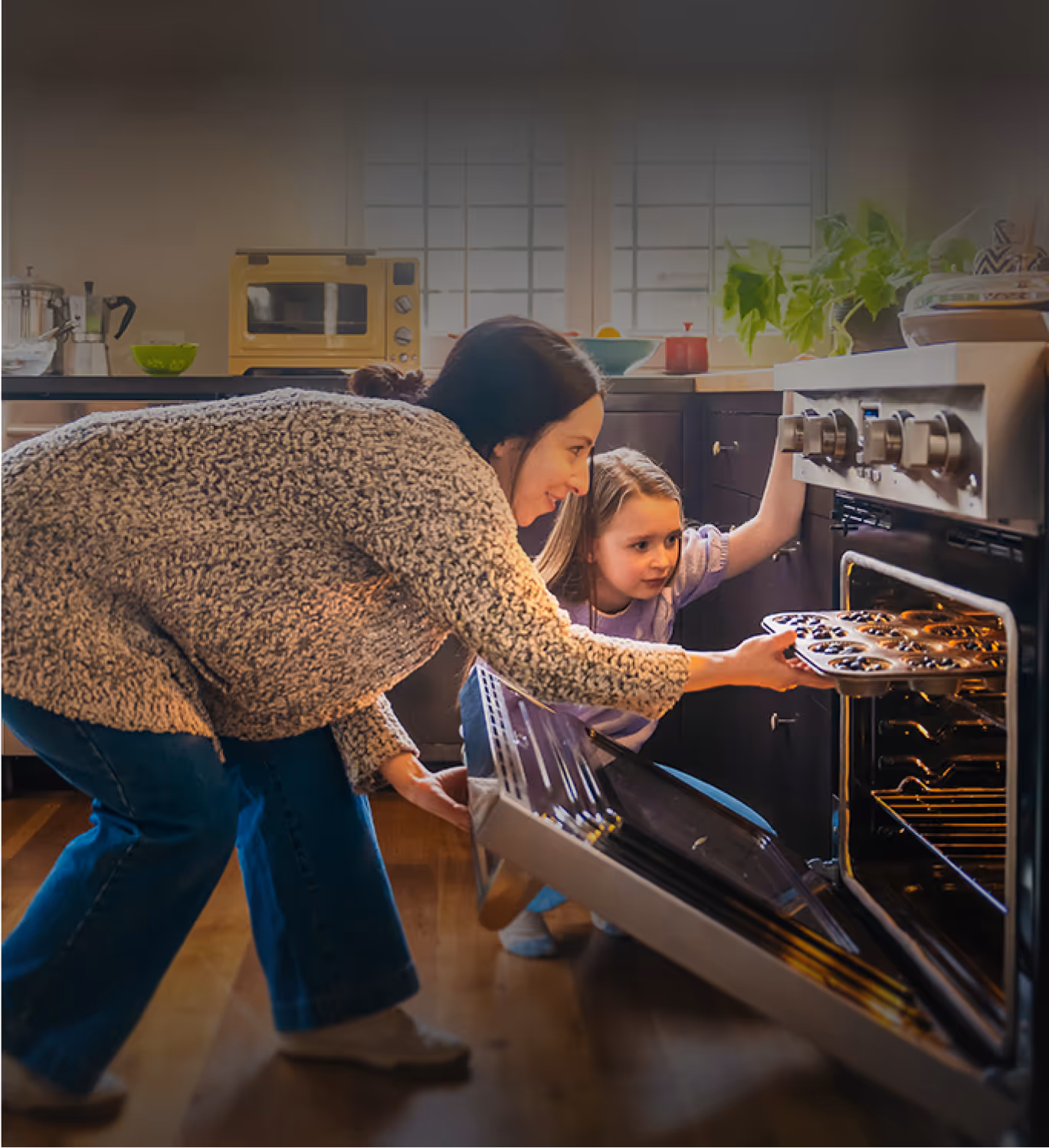 A mother and daughter pulling muffins out of the oven