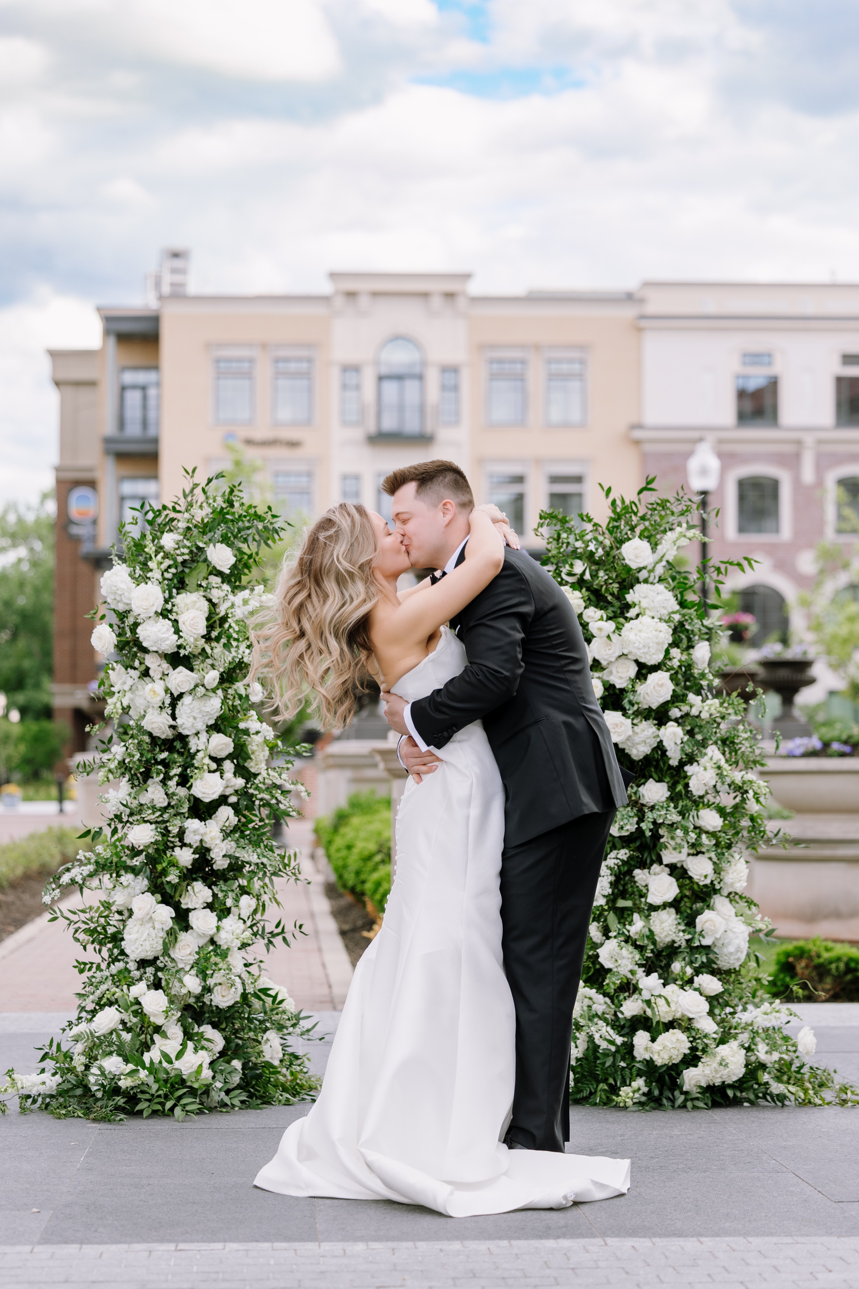 bride and groom kissing in front of floral installation at carmichael hotel