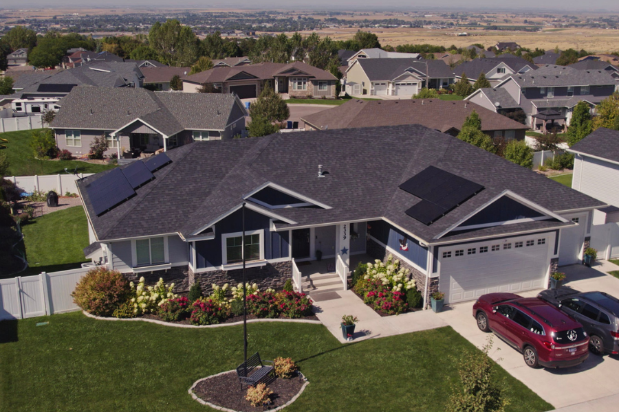Aerial view of a residential neighborhood with a modern home featuring rooftop solar panels installed by Big Dog Solar in the front and back sections of the roof.