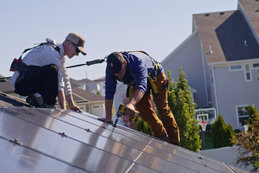 Two Big Dog Solar technicians installing solar panels on a residential rooftop in Grand Junction, Colorado, using power tools and safety harnesses.