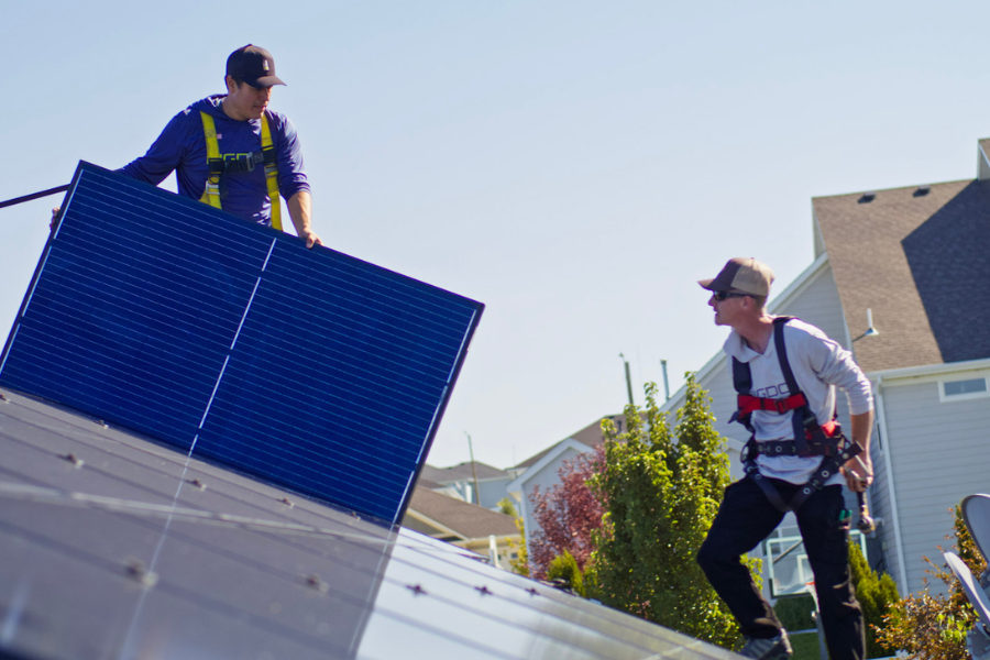 Big Dog Solar Energy technicians carrying and installing a solar panel on a residential roof.