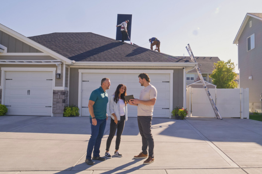 Big Dog Solar Energy team discussing a residential solar project with homeowners while installers work on the roof.