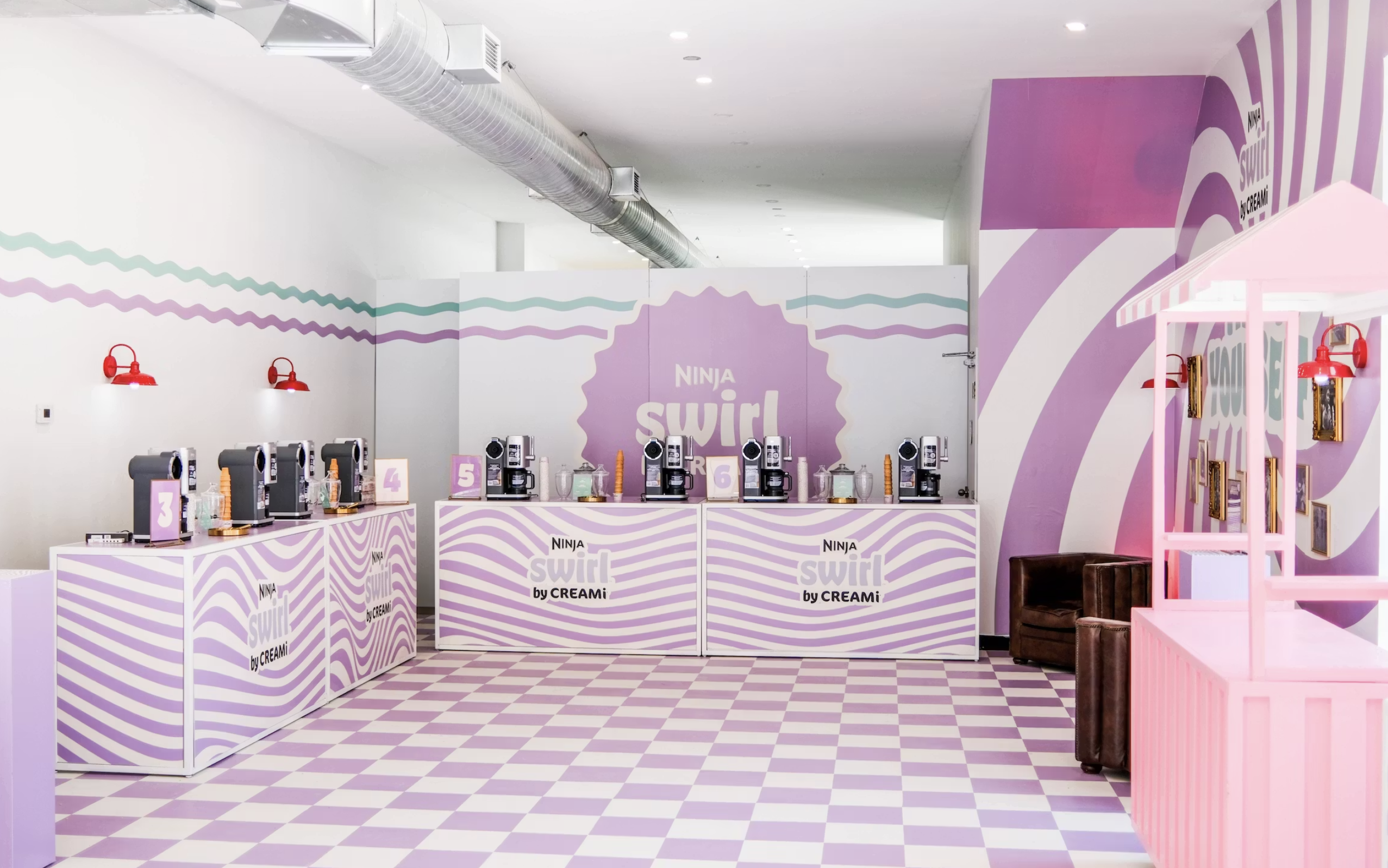 Bright room with purple and white checkered floor, counters with Ninja Swirl by Creami machines, and pink accents including a small stand and red wall lamps.