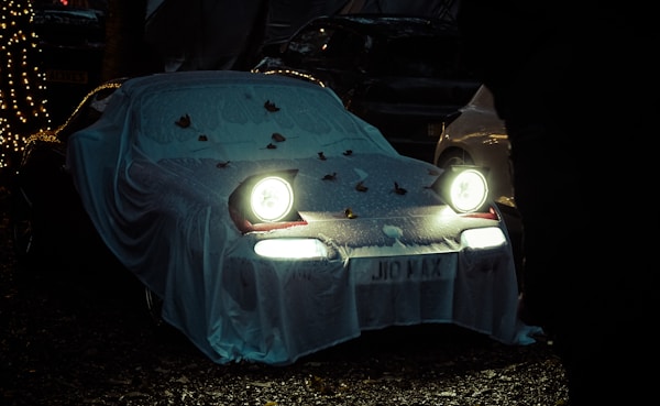 A Car with a blanket laid on top to look like a ghost with headlights.