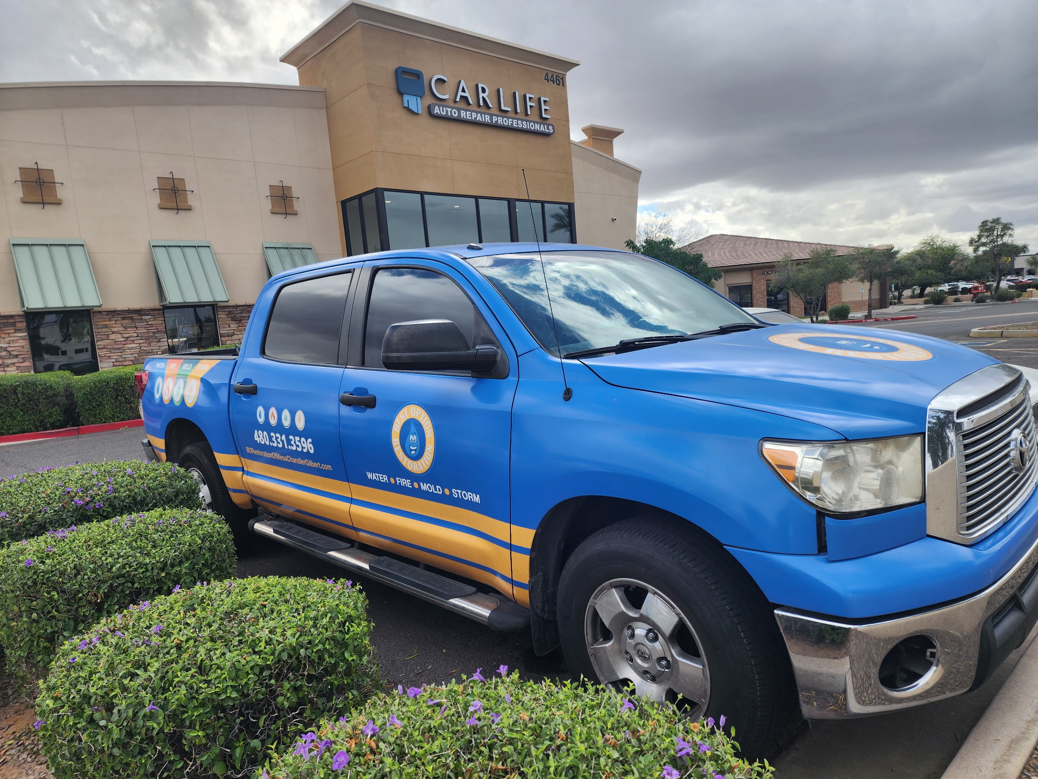 Blue restoration company truck parked outside CarLife auto repair shop on a cloudy day.
