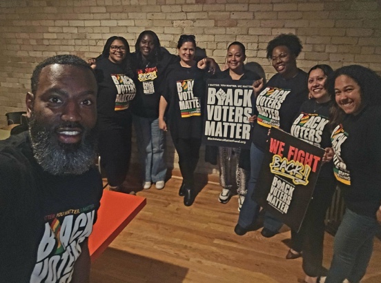 Group of seven diverse people indoors wearing Black Voters Matter shirts and holding signs that say 'Black Voters Matter' and 'We Fight Back!'