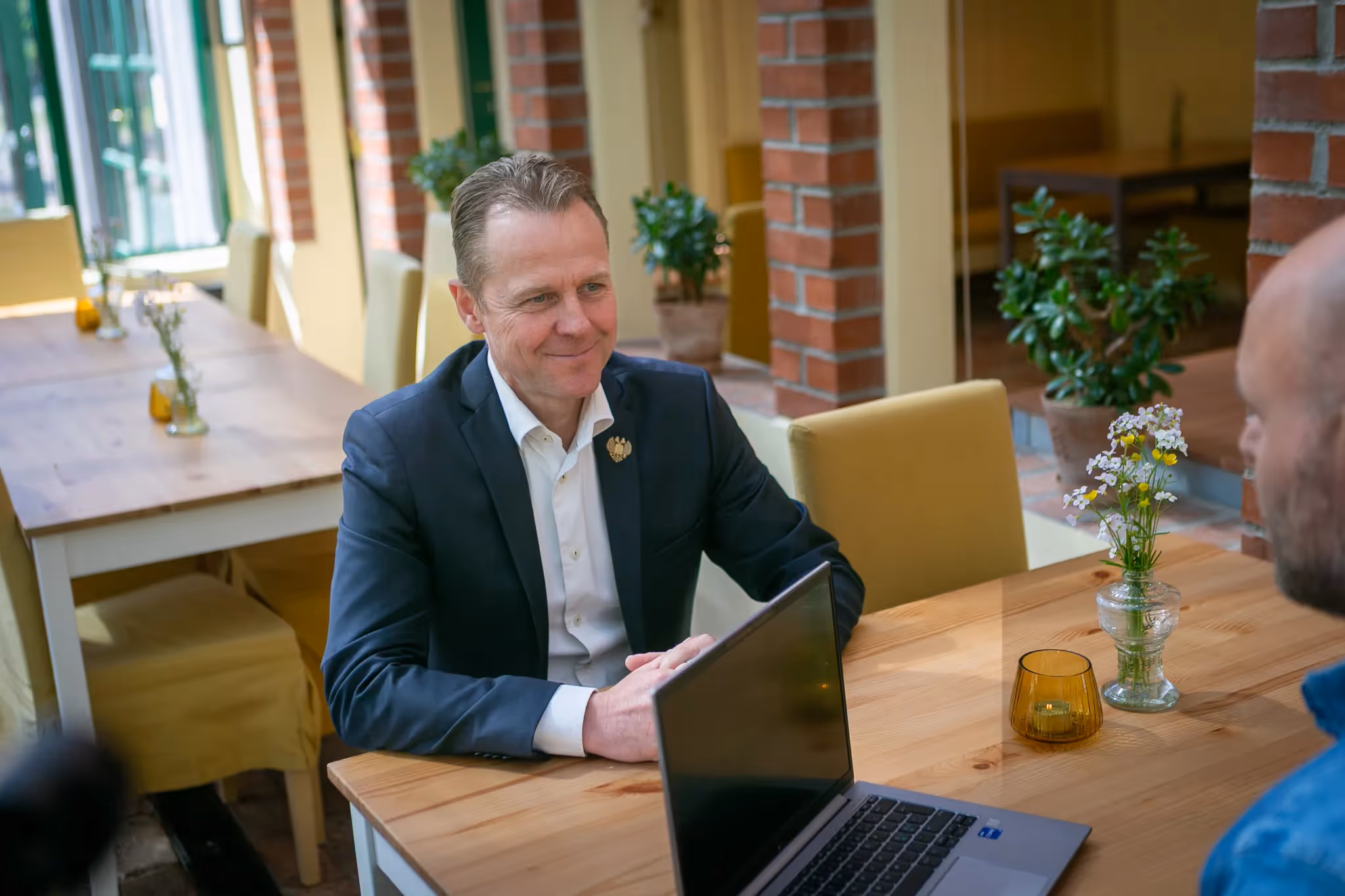 To menn som har et møte rundt et bord med blomster og en bærbar pc. 
