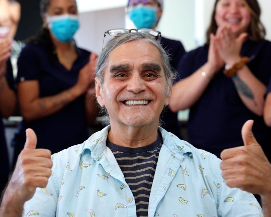 Smiling man after dental implants with people clapping behind him