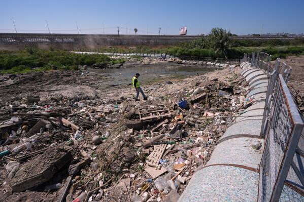 Oscar Romo walks among debris that has been captured by a trash boom installed in the Tijuana River at the border near where the river enters the United States from Tijuana, Mexico, Wednesday, April 8, 2026, in San Diego, Calif. (AP Photo/Gregory Bull)