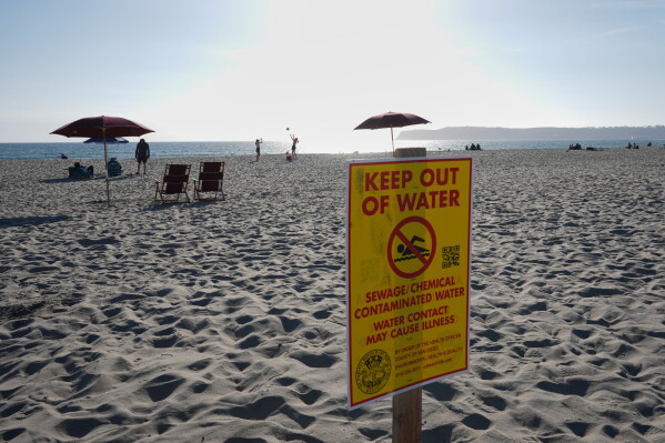 A sign warns of sewage and chemical contaminated water along a beach Tuesday, March 10, 2026, in Coronado, Calif. (AP Photo/Gregory Bull)