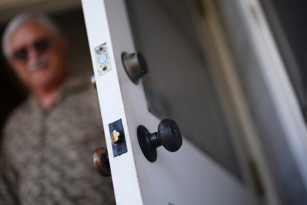 Steve Egger looks out from his door where the outer doorknob has turned black at his home Friday, March 6, 2026, in San Diego. (AP Photo/Gregory Bull)