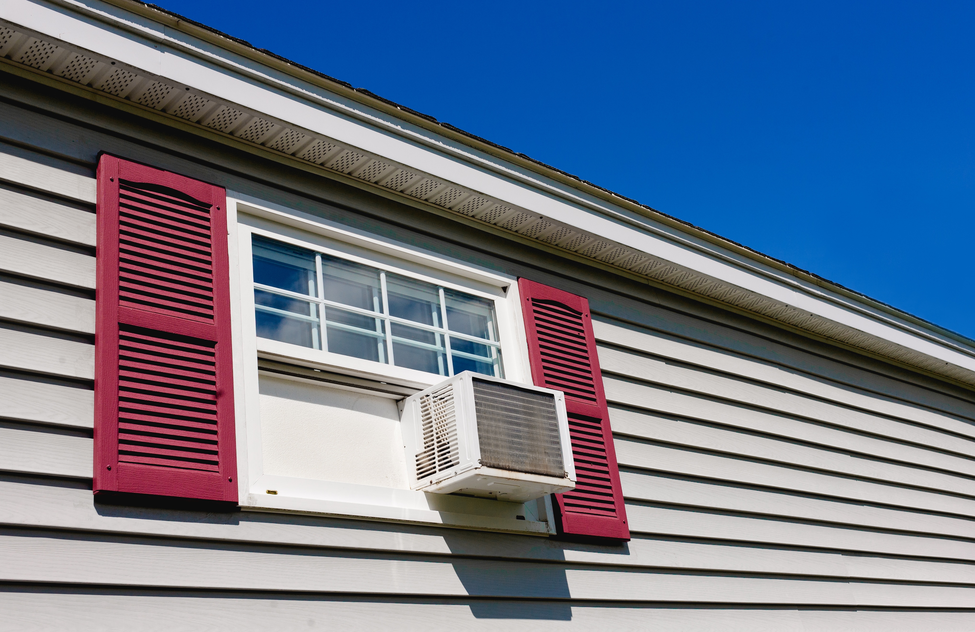 Window air conditioner installed on a suburban house with red siding and white windows