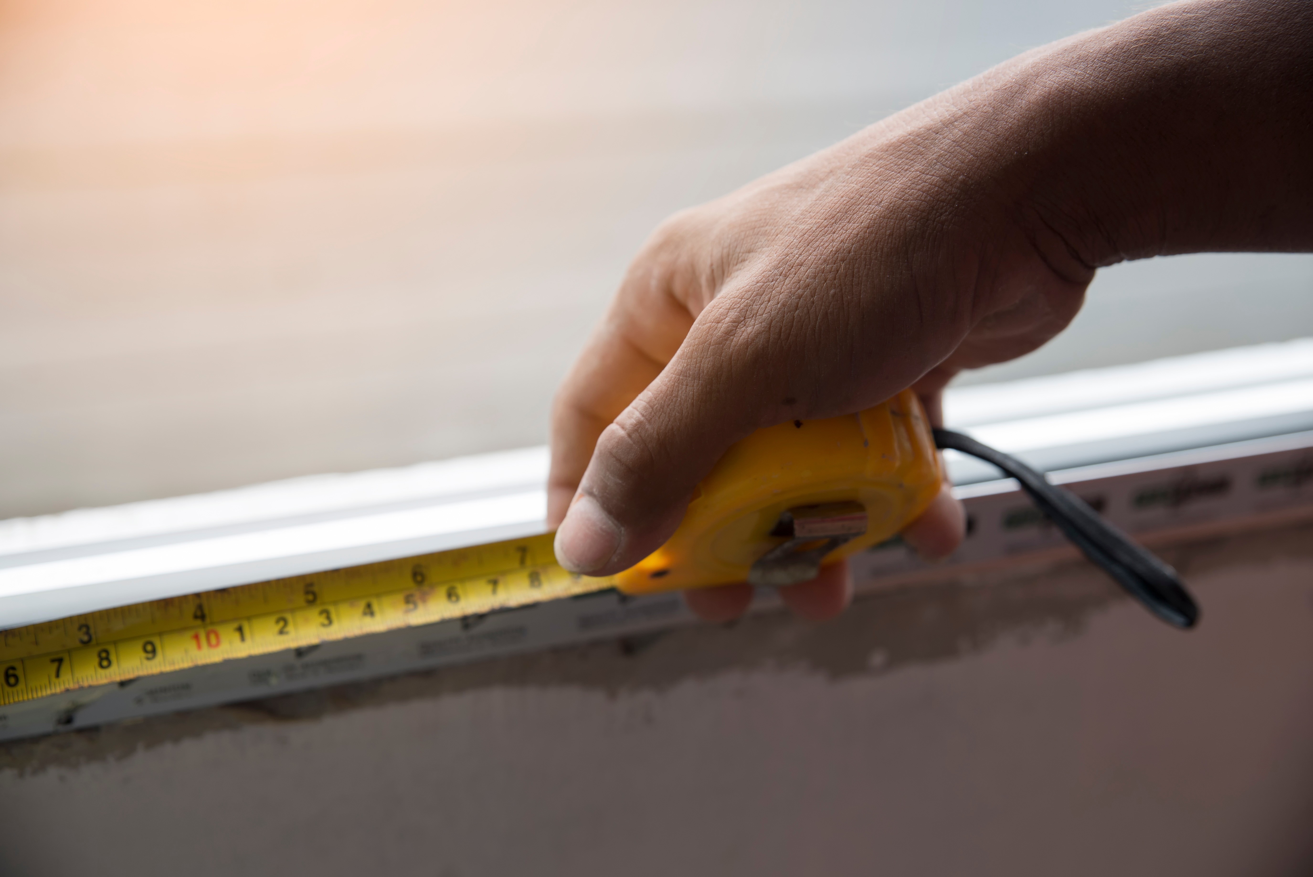 Person using a tape measure to measure the dimensions of a window