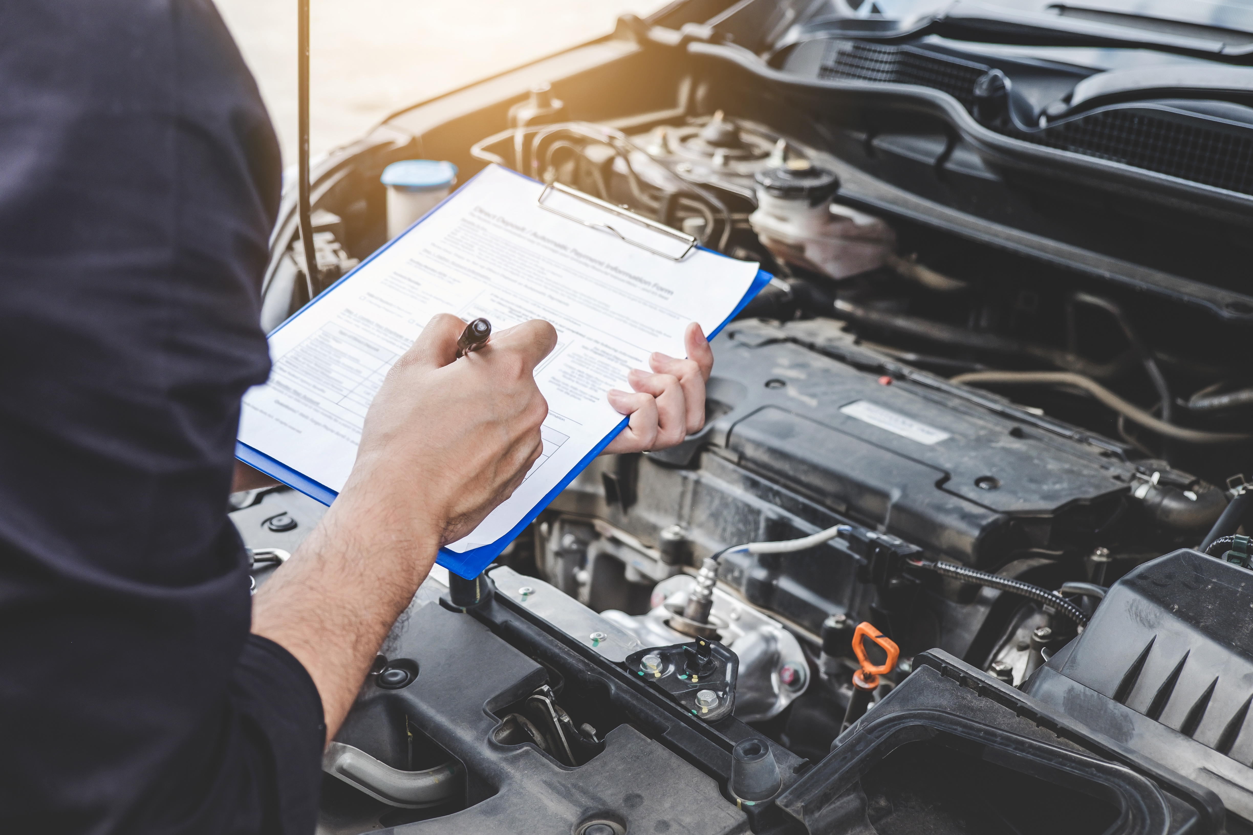 Person holding a clipboard while doing a diagnostic check on a car