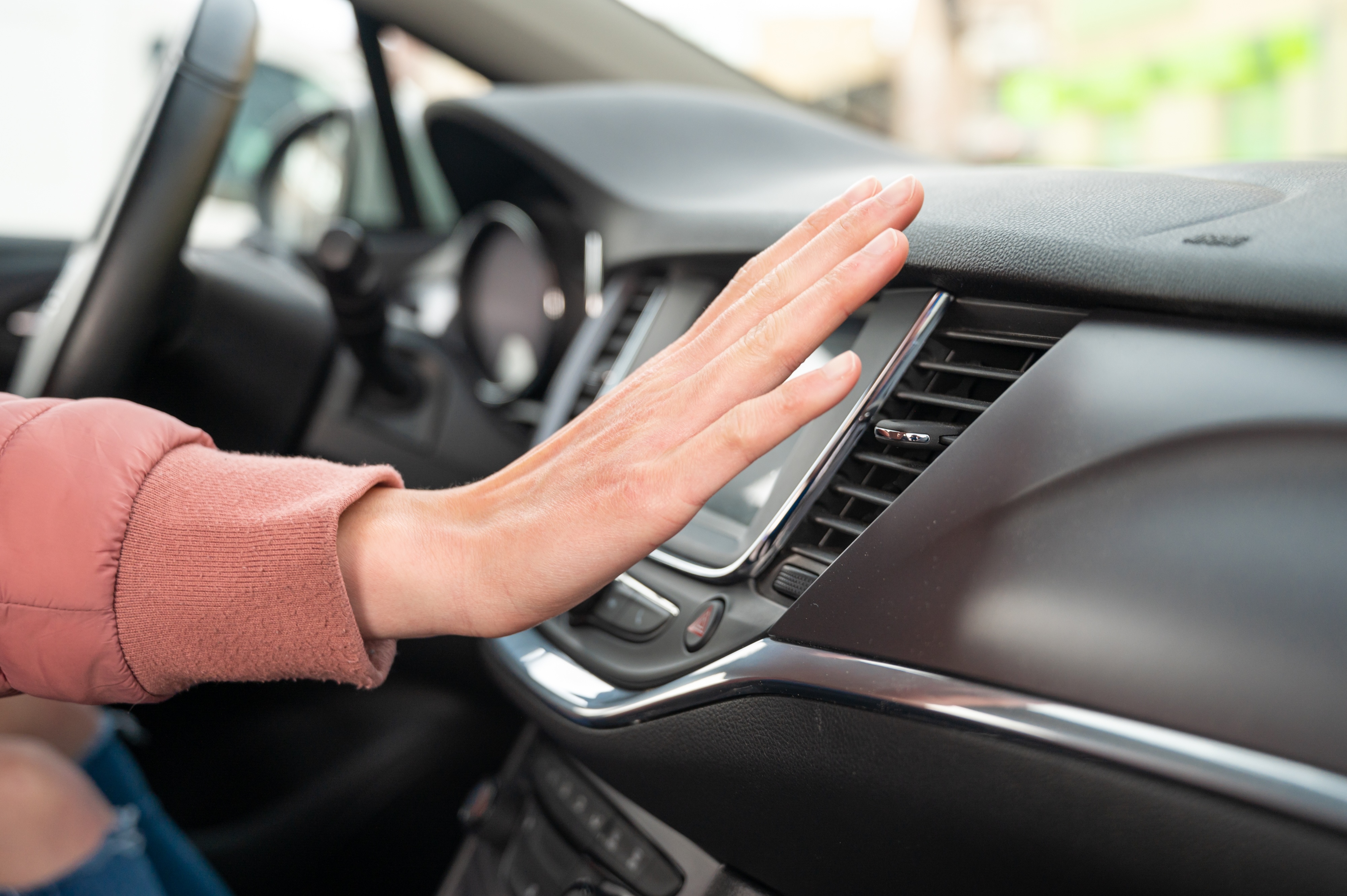 Someone wearing a red sweater sticking their hand in front of the a/c unit in a car to stay cool