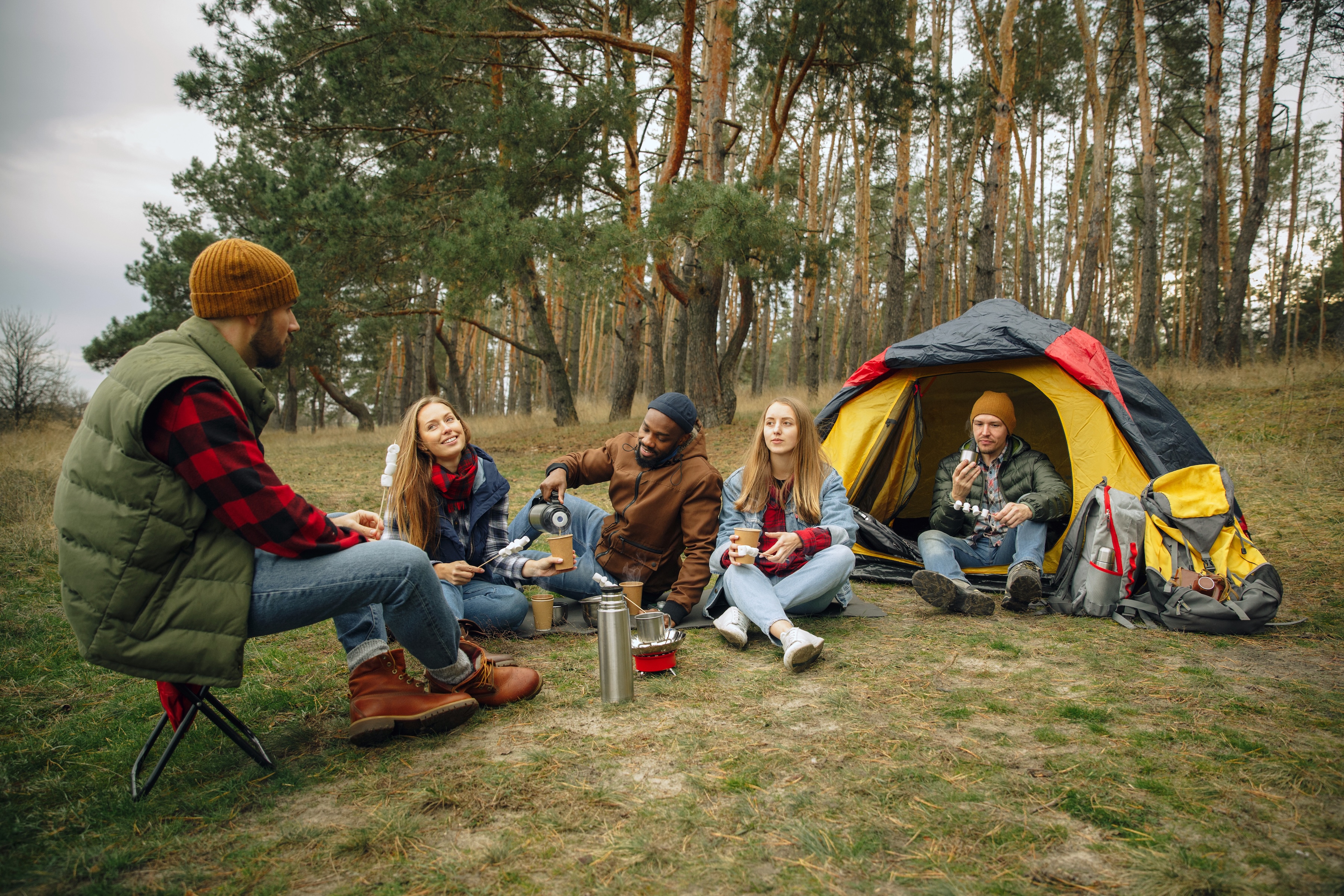 Group of friends sitting out in the woods while camping and drinking coffee