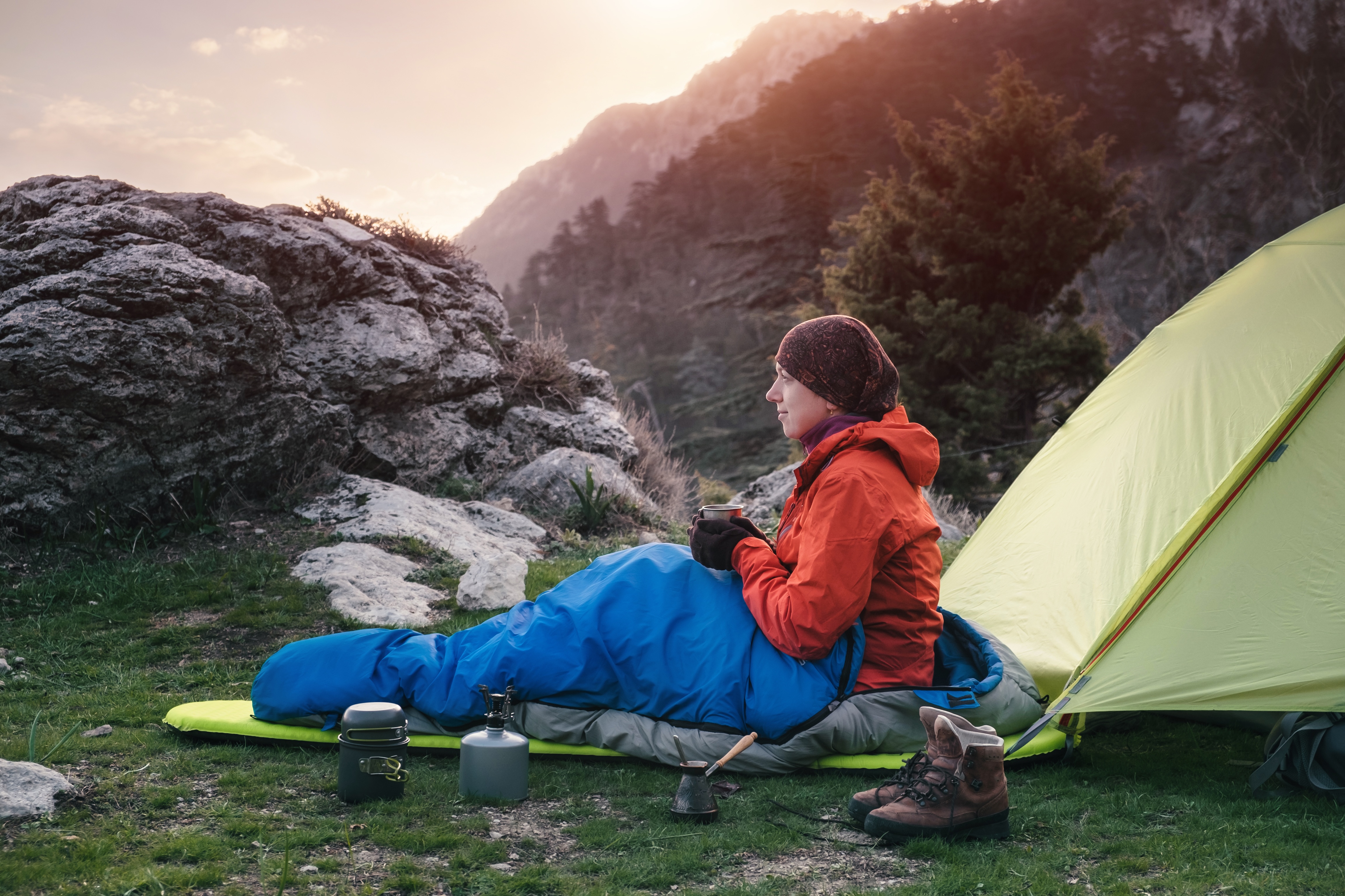 woman in an orange coat sitting in a blue sleeping bag while camping in the mountains