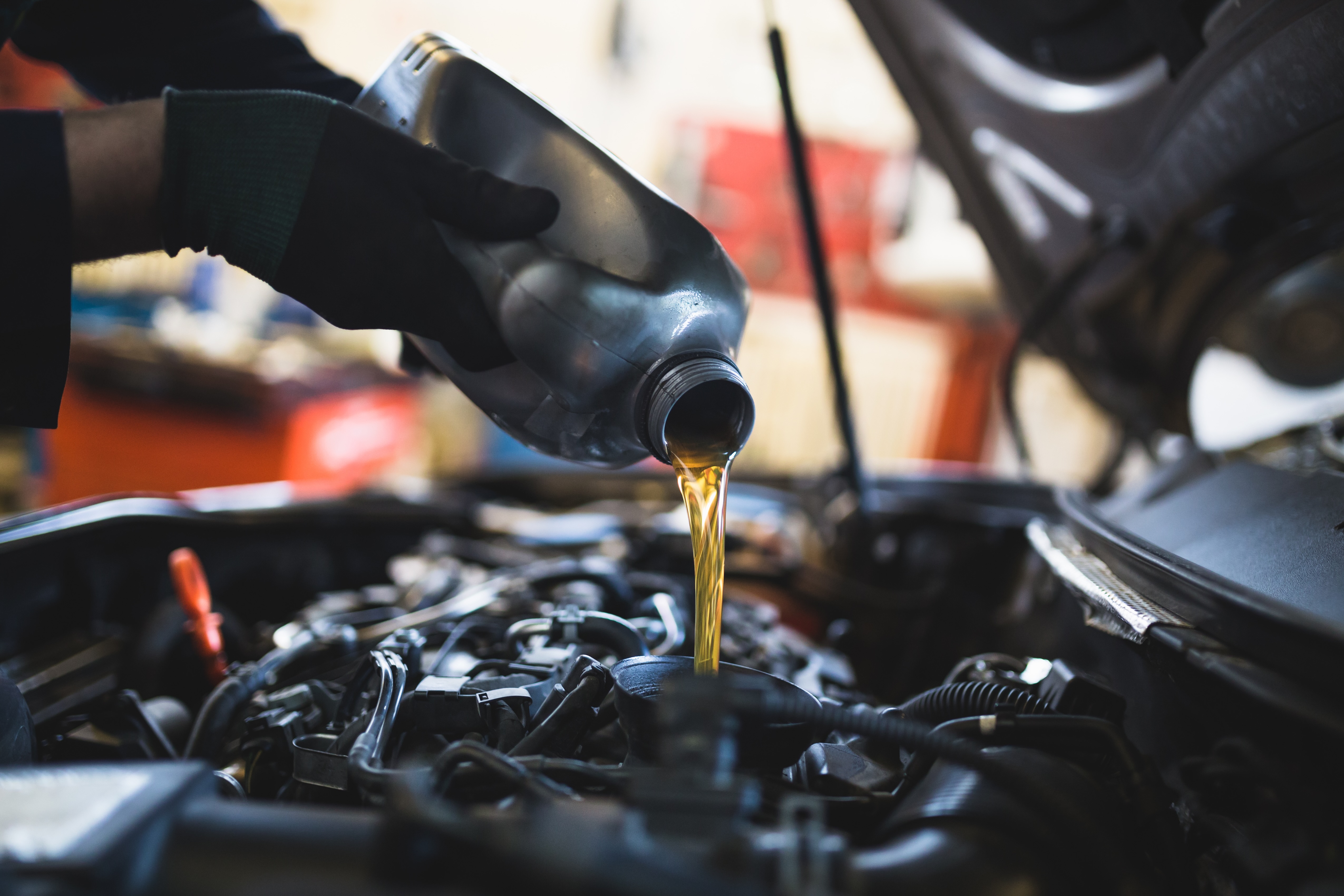 Person wearing gloves pouring oil under the hood of a car