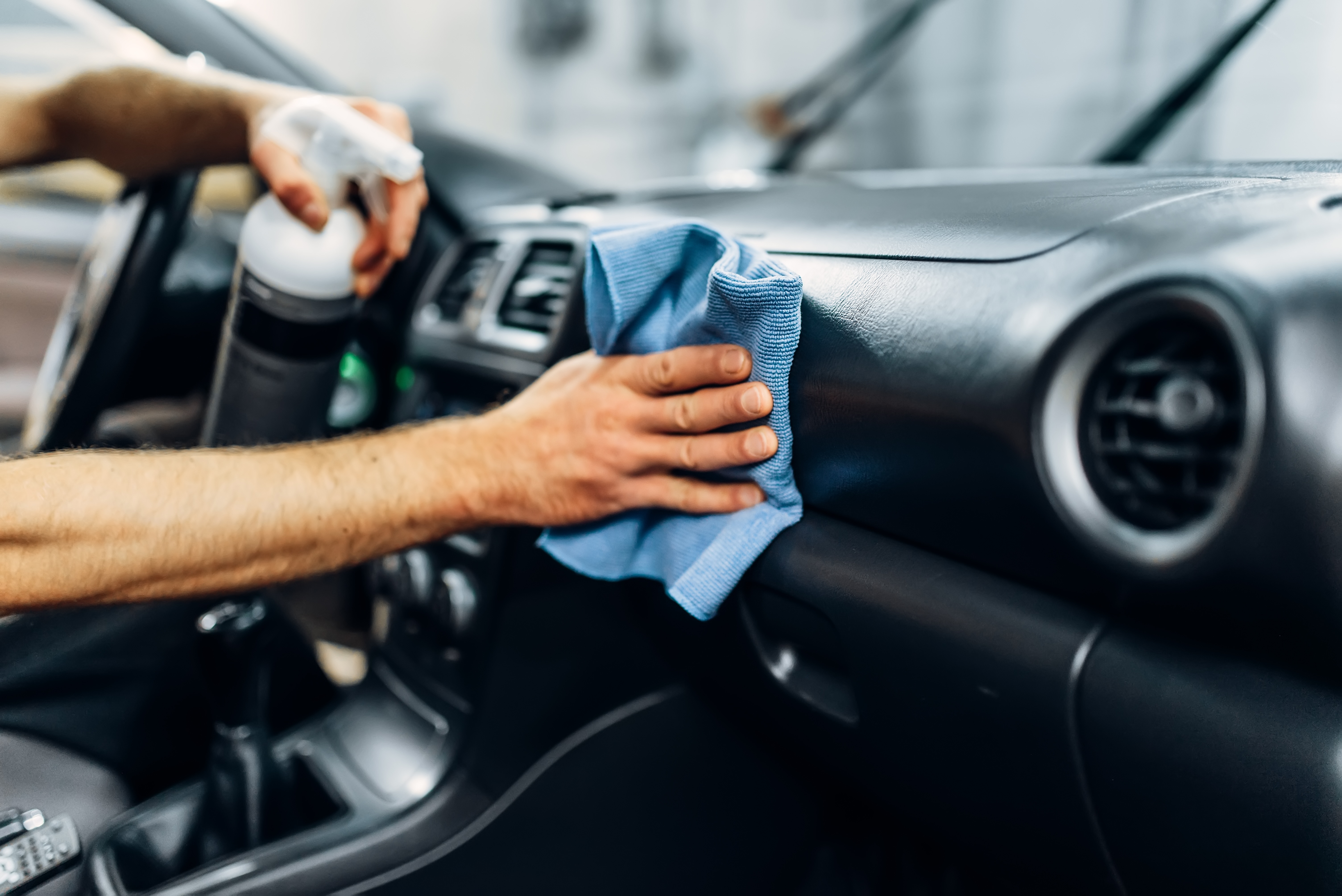 Person using a cloth and spray to clean the interior of a car