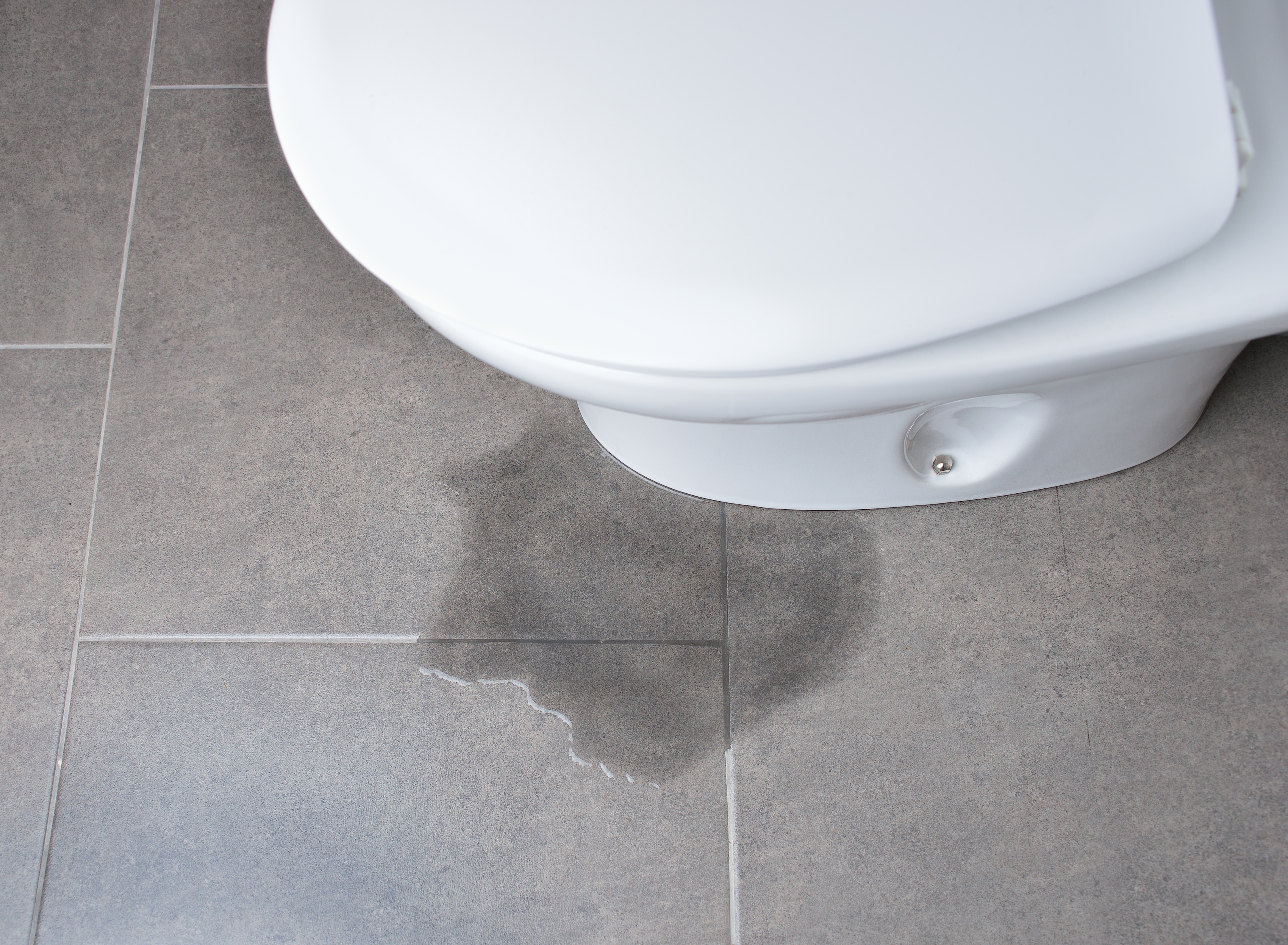 Toilet with leaking water coming out of the base onto a tile floor