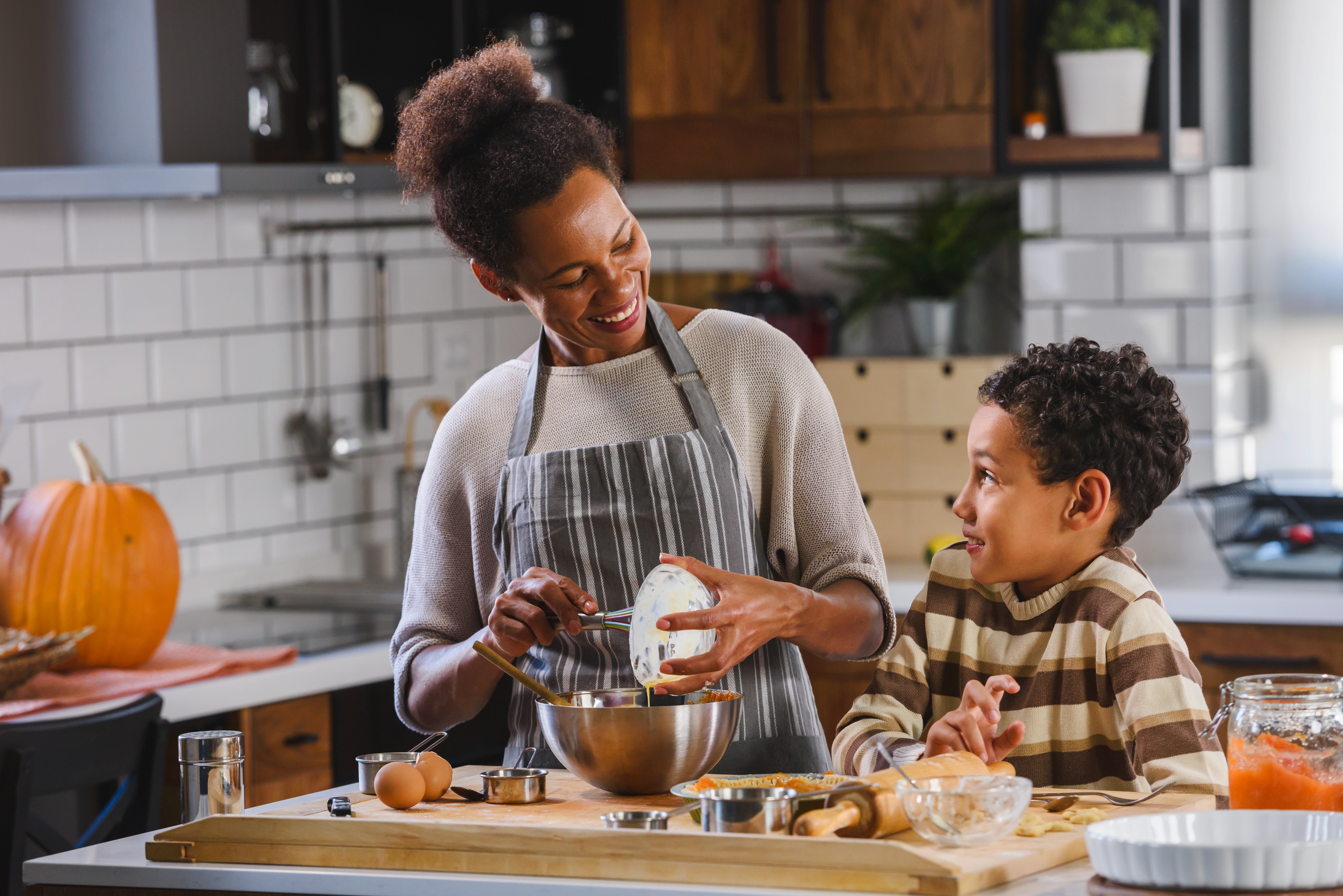 Mother and son in the kitchen baking fall treats with a pumpkin in the background