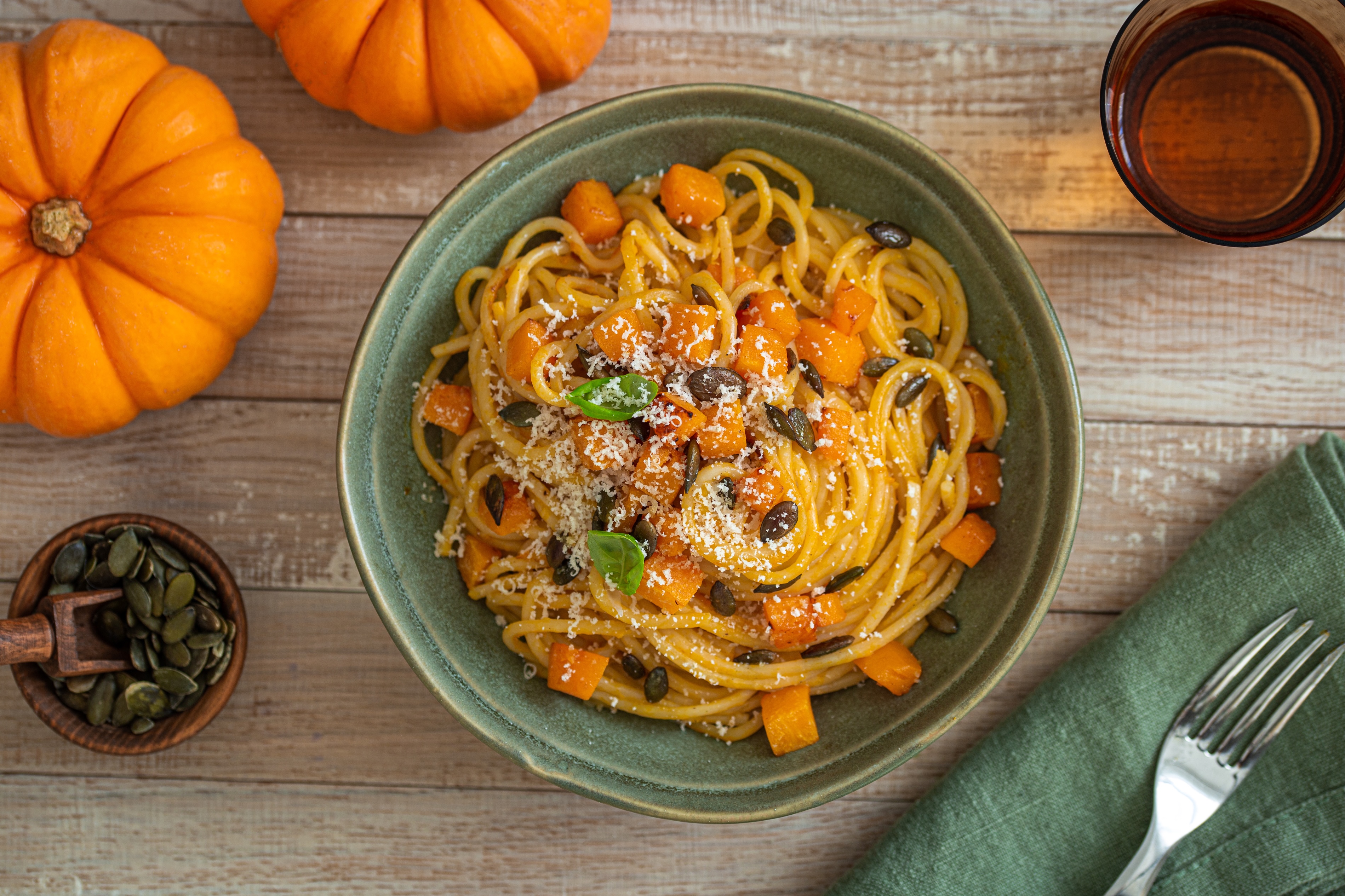Bowl of pumpkin-flavored spaghetti in a green bowl on a wooden table with pumpkins surrounding
