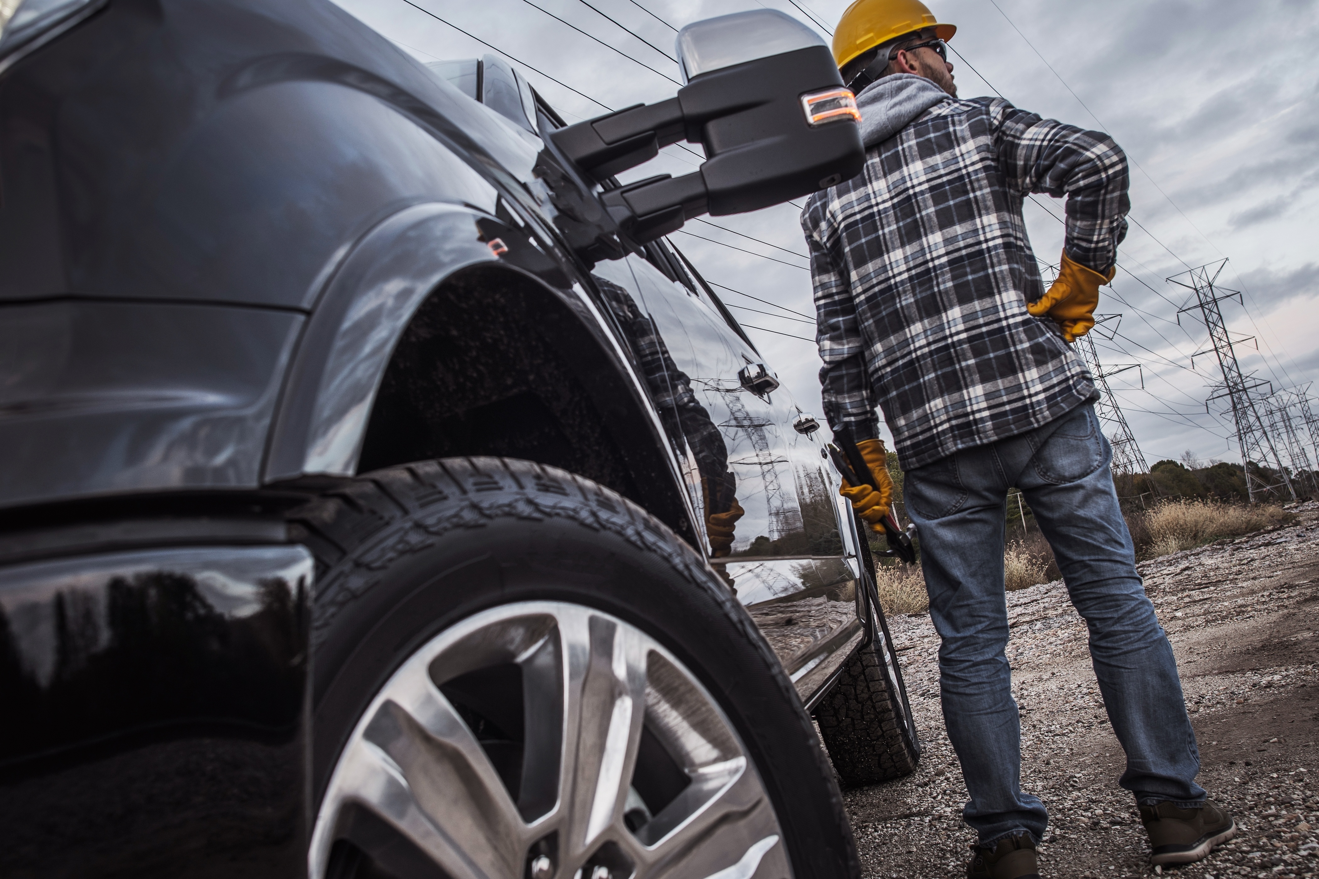 Man standing by a black truck wearing workwear and a hard hat on a cloudy day