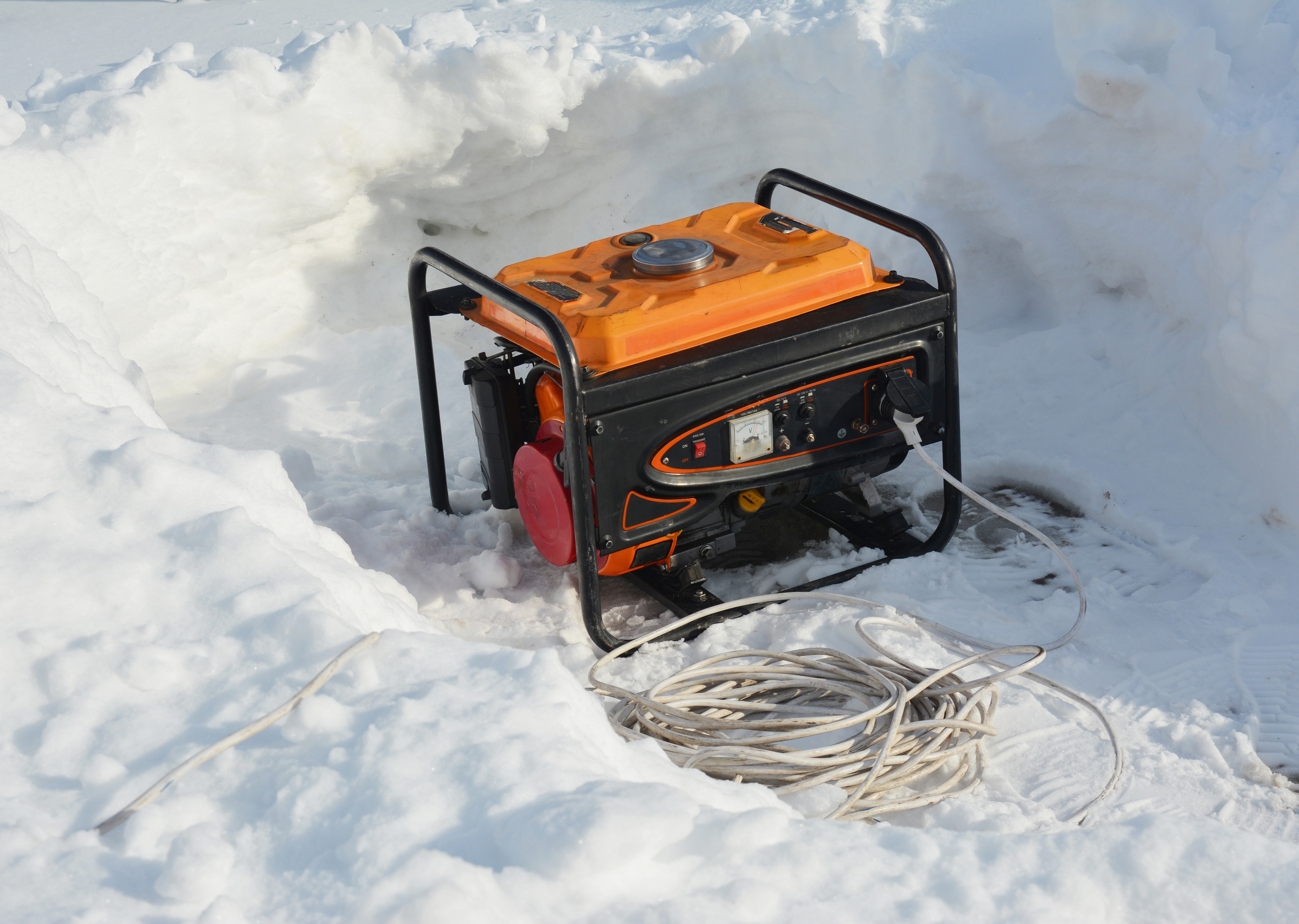Orange and black portable generator sitting in a shoveled out area of snow