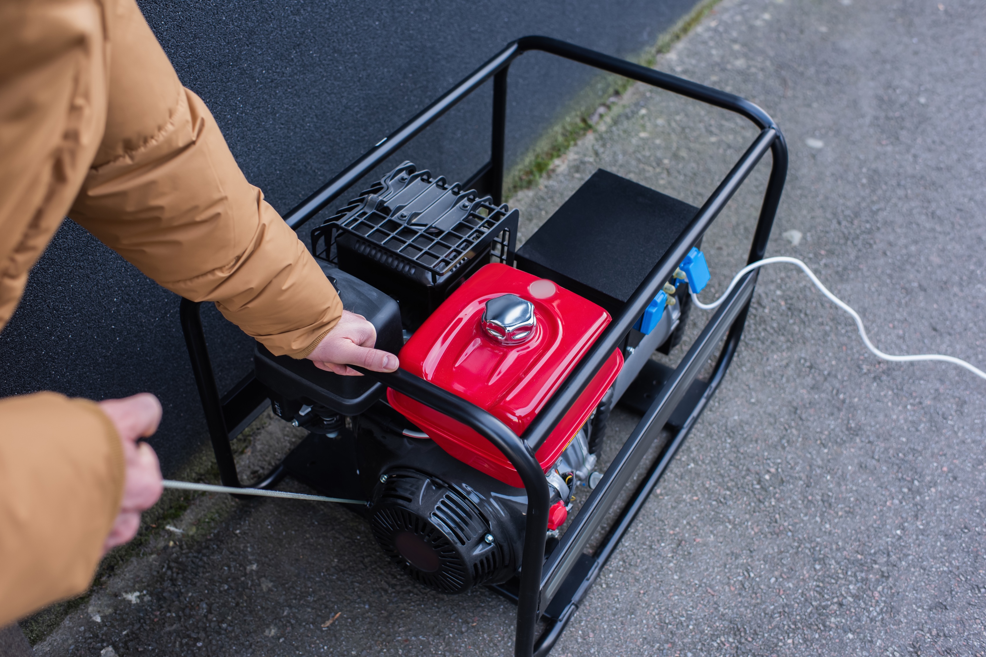 Man in a brown coat using a cord to start up a portable generator during a power outage