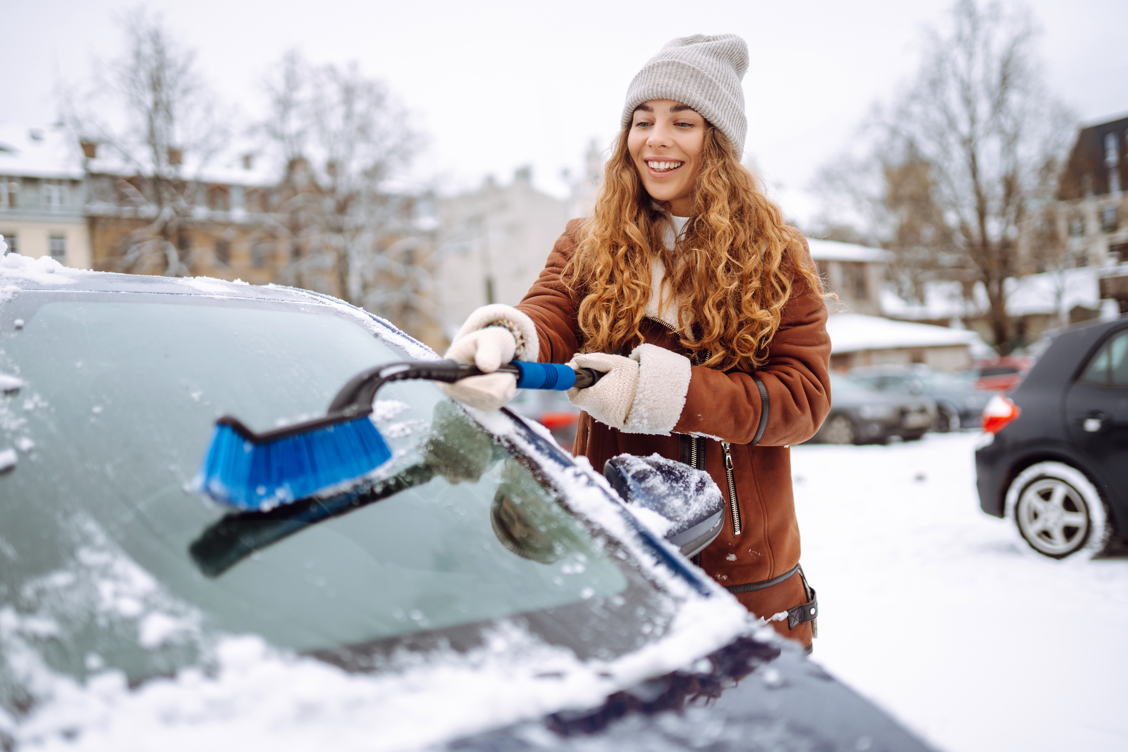 A woman using a snow brush to clear snow off of her car