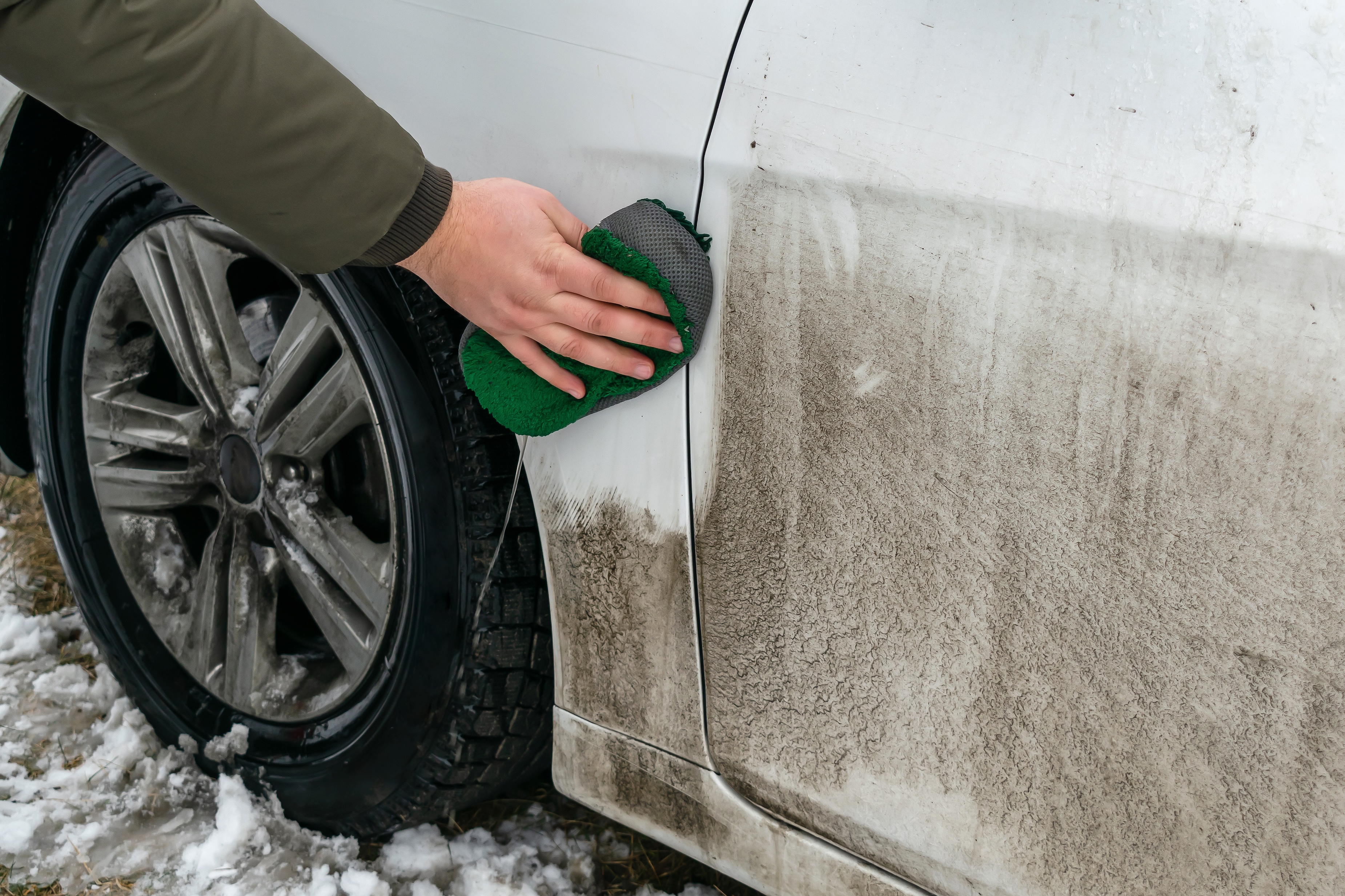 Man cleaning dirt automobile with rag at home backyard outdoor winter snowy day