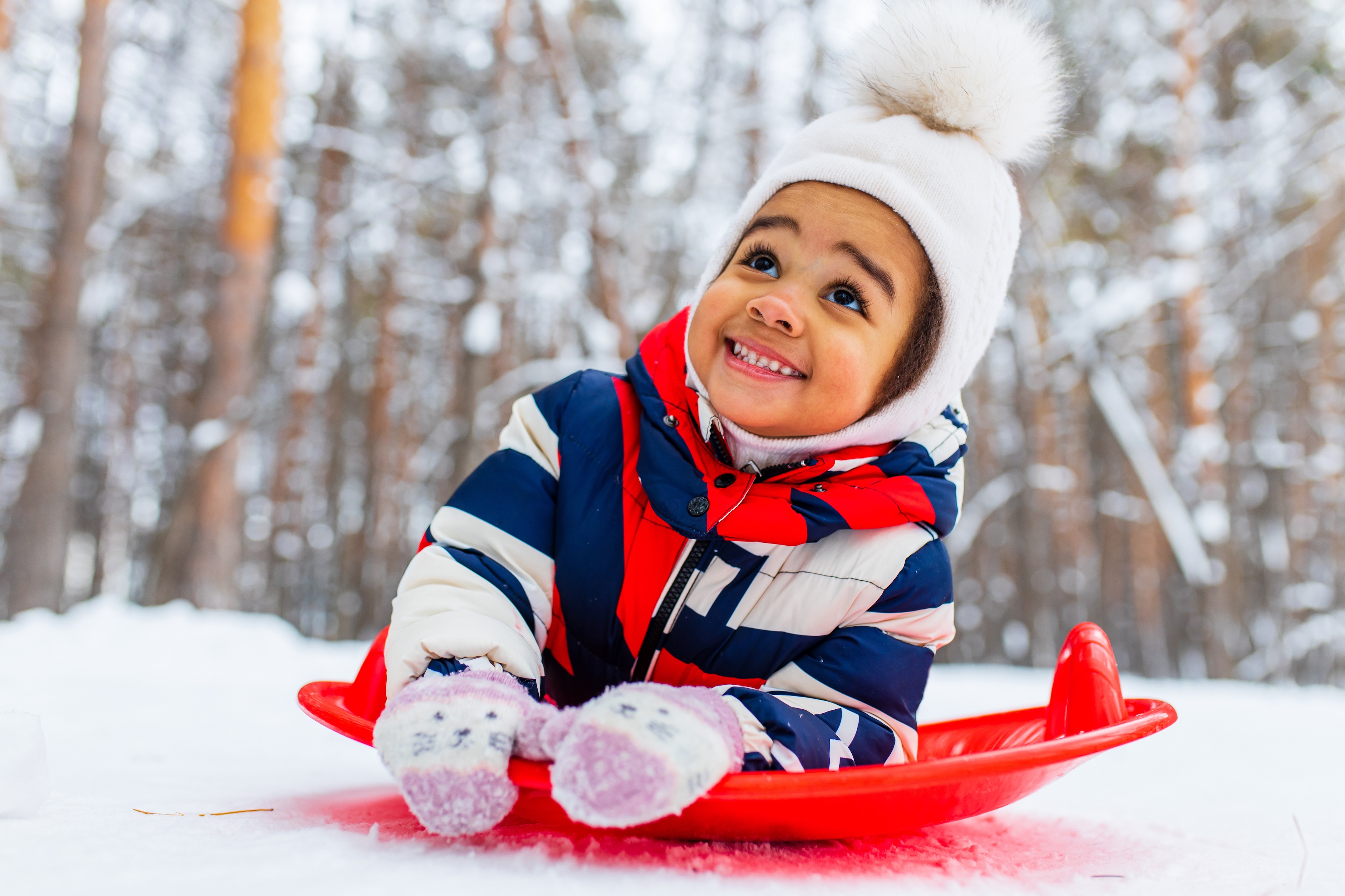 Child bundled up and playing on a red saucer sled in the snow