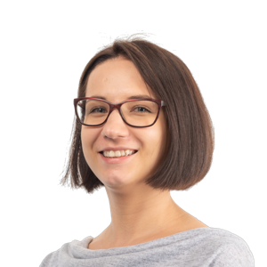 Smiling woman with short dark hair wearing glasses and a gray shirt against a white background.