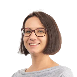 Smiling woman with short dark hair wearing glasses and a gray shirt against a white background.