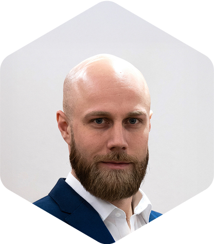 Professional headshot of a bald man with a full beard wearing a dark blue jacket and white shirt against a light gray background.
