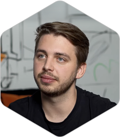 Portrait of a man with dark hair and facial hair wearing a black shirt, photographed indoors with blurred background.