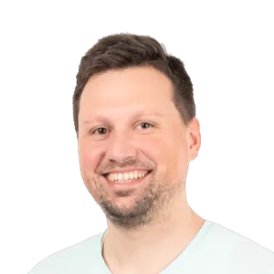 Headshot of a smiling man with brown hair and facial hair wearing a light blue shirt against a white background.