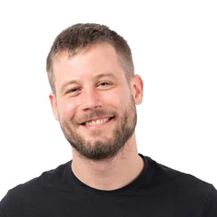 Headshot of a smiling man with short brown hair and beard wearing a black t-shirt against a white background.