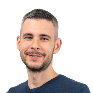 Headshot of a smiling man with short dark hair and facial hair wearing a dark blue shirt against a white background.