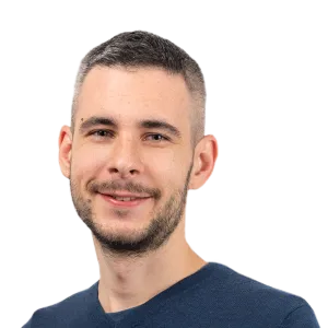 Headshot of a smiling man with short dark hair and facial hair wearing a dark blue shirt against a white background.