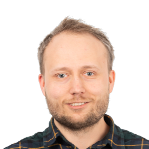 Headshot of a smiling man with light brown hair and beard wearing a dark checkered shirt against a white background.