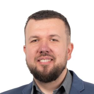 Professional headshot of a man with dark hair and beard wearing a dark blue blazer and dark shirt against a white background.