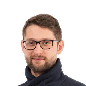 Headshot of a man with glasses and beard wearing a dark navy sweater against a white background.