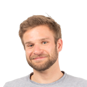 Headshot of a smiling man with light brown hair and beard wearing a gray t-shirt against a white background.