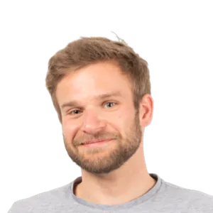 Headshot of a smiling man with light brown hair and beard wearing a gray t-shirt against a white background.