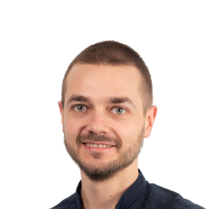 Professional headshot of a smiling man with short brown hair and facial hair, wearing a dark blue shirt against a white background.